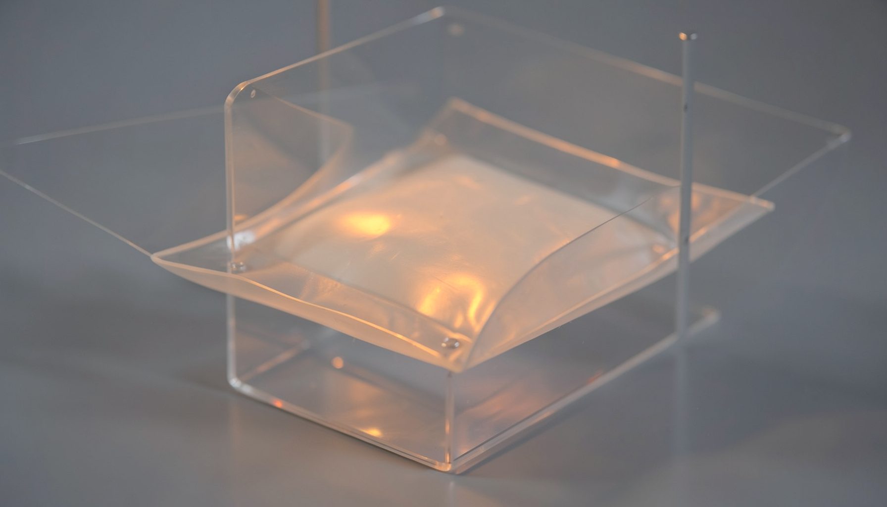 A softly lit membrane module with faint amber reflections on its surface, suspended in a transparent housing.